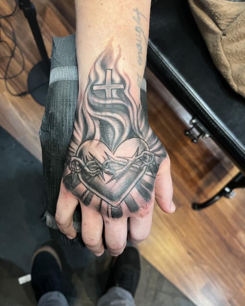 Black and grey sacred heart with flames, chain and cross on a hand